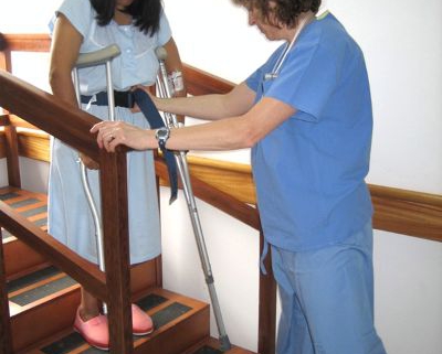 A CAMTA member helping a patient walk down the stairs using crutches